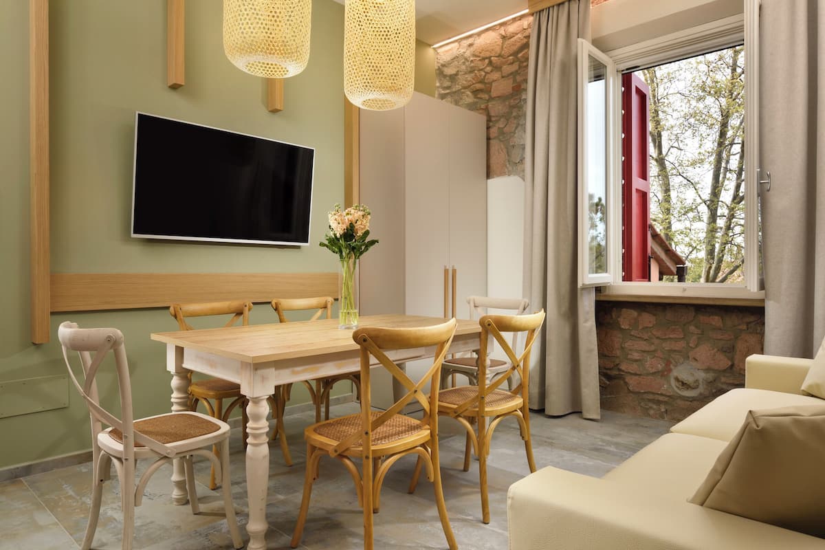 A dining area with a wooden table and chairs, a flat-screen TV mounted on the wall, and a stone wall with a window.