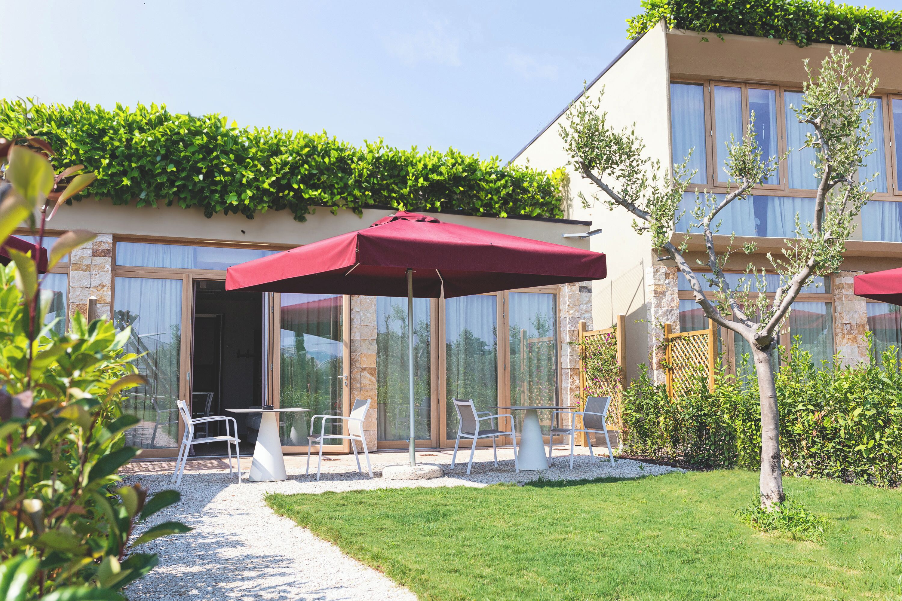 A modern building with a patio area featuring outdoor seating and a red umbrella.