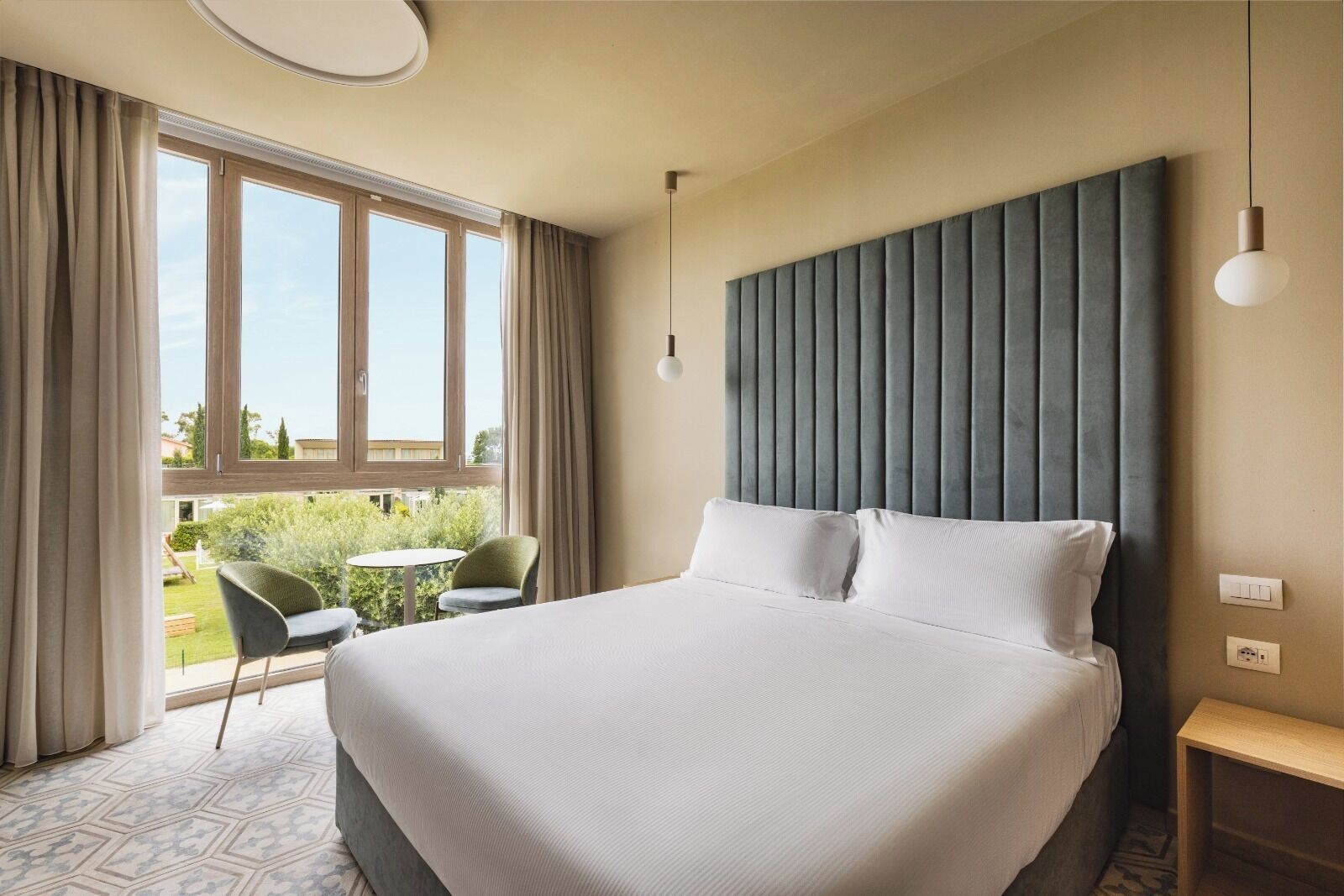 Ein Hotelzimmer mit einem großen Bett, einem Fenster mit Vorhängen, einem kleinen Tisch und einem Stuhl.