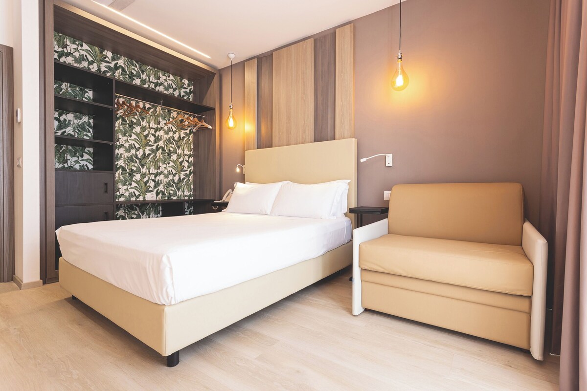 Quarto moderno com uma cama grande, um sofá, um guarda-roupa e uma parede com padrão de folhas.
