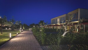 A nighttime view of a hotel with a paved walkway, outdoor seating area, and a water feature. - San Francesco Country Resort (Rosignano Marittimo)