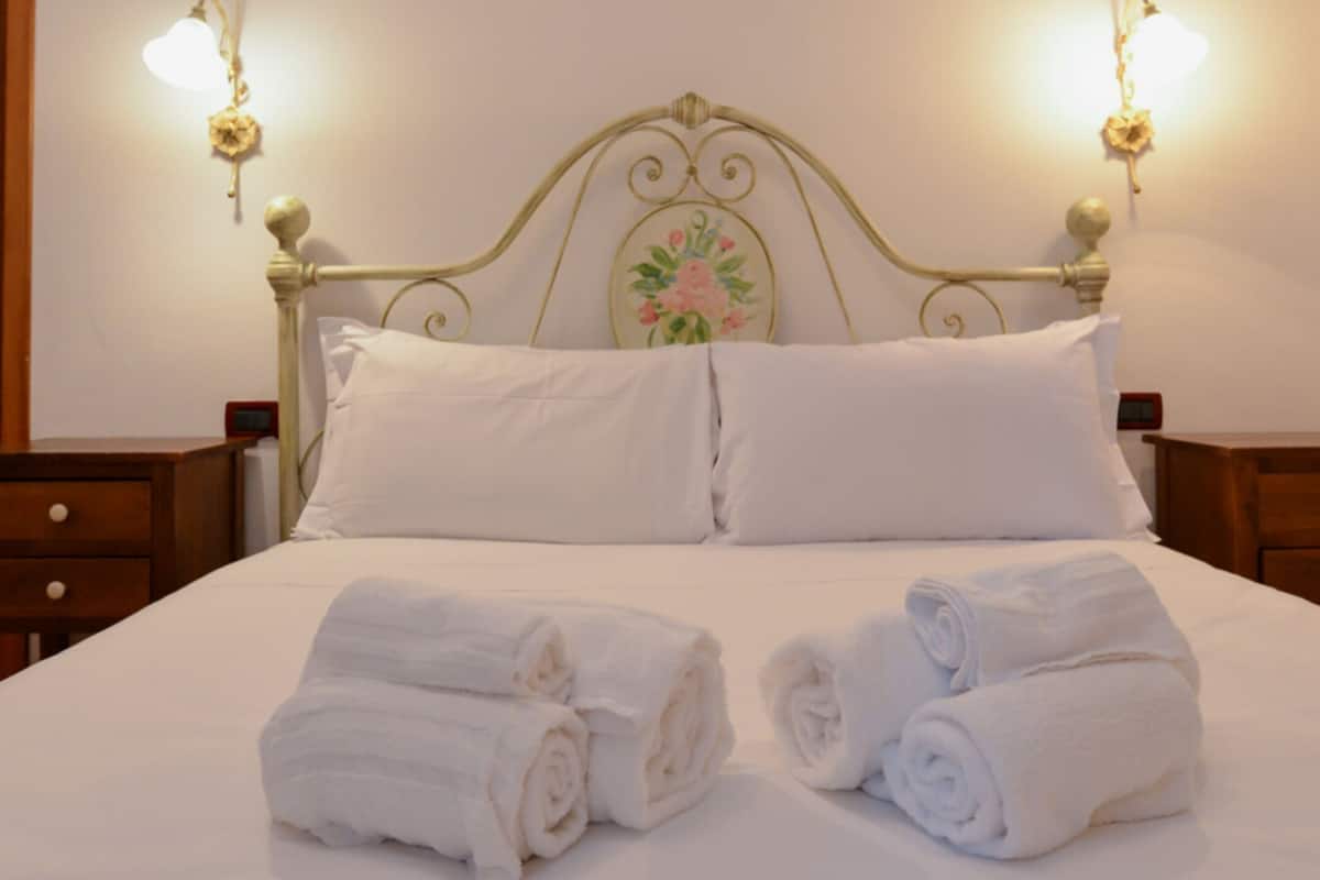 A neatly made bed with white linens and two rolled towels on the bed.