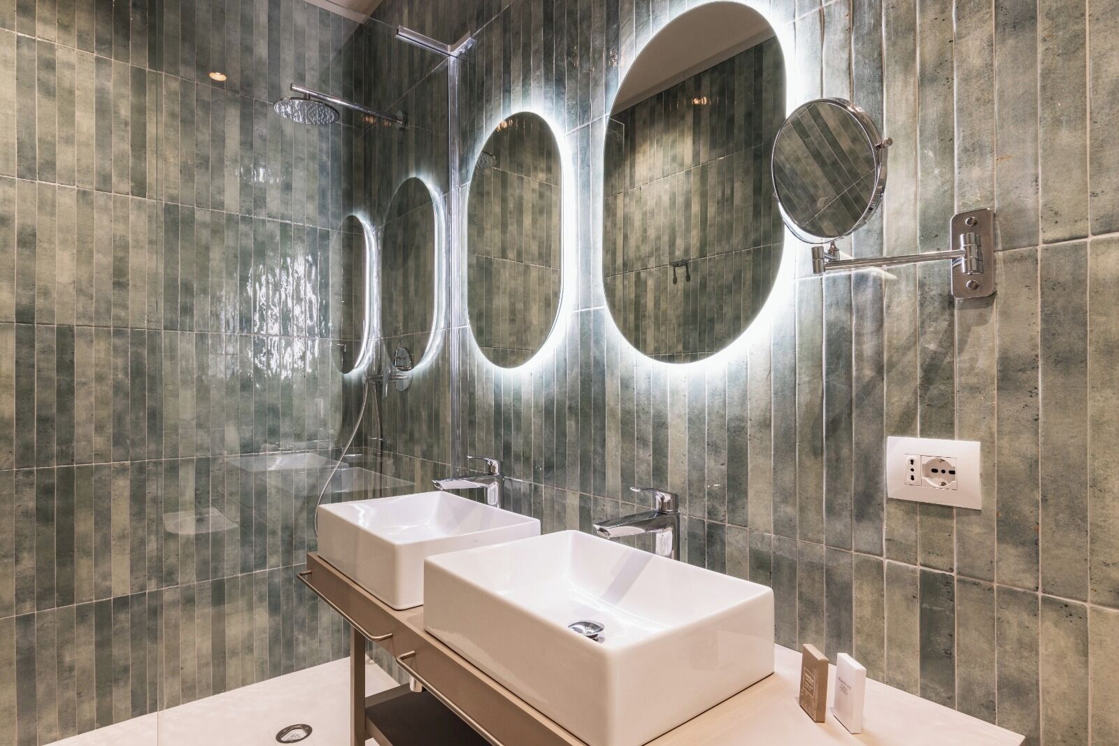 A modern bathroom with two sinks, a shower, and three mirrors.