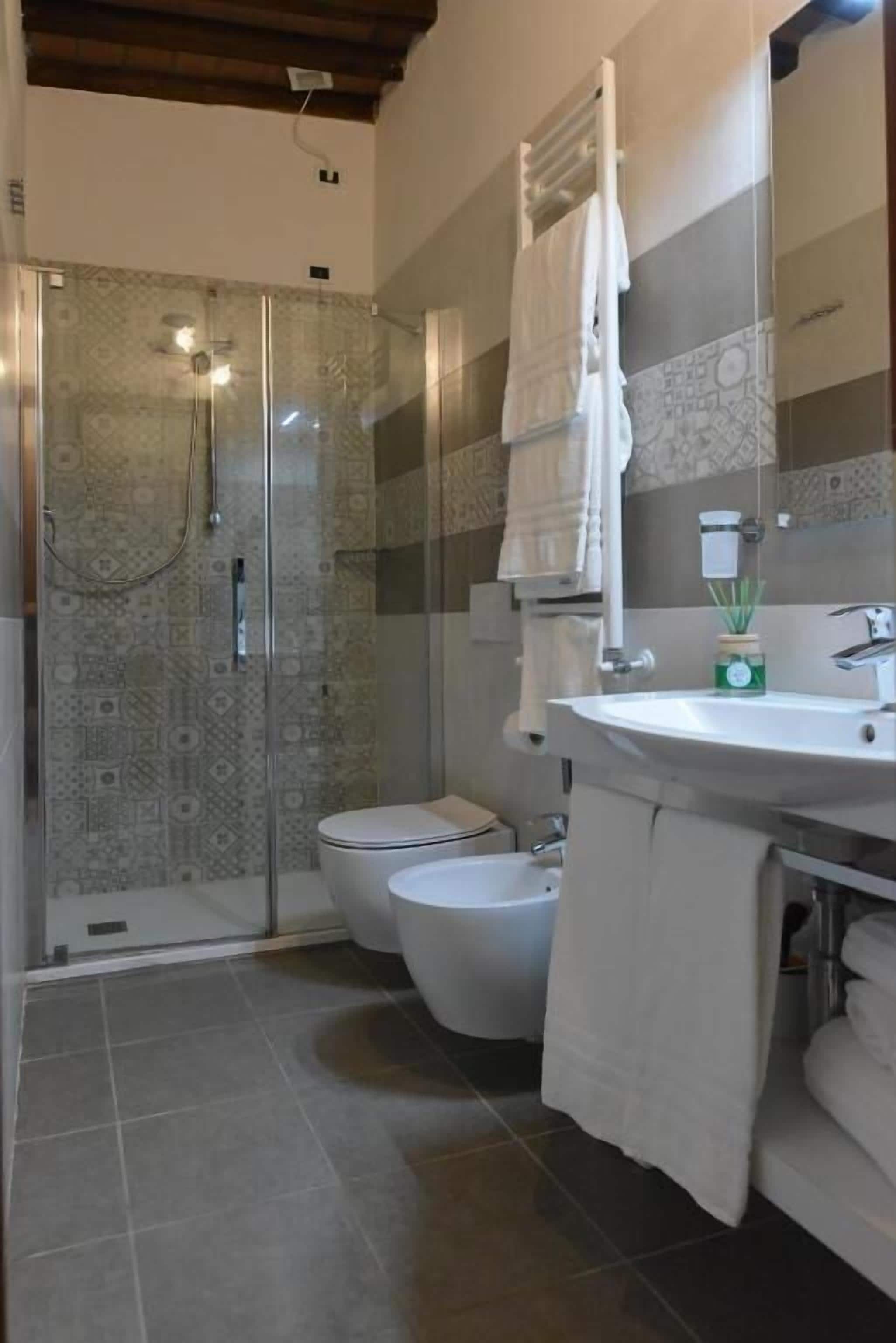 A bathroom with a glass-enclosed shower, a toilet, and a sink with a towel rack.