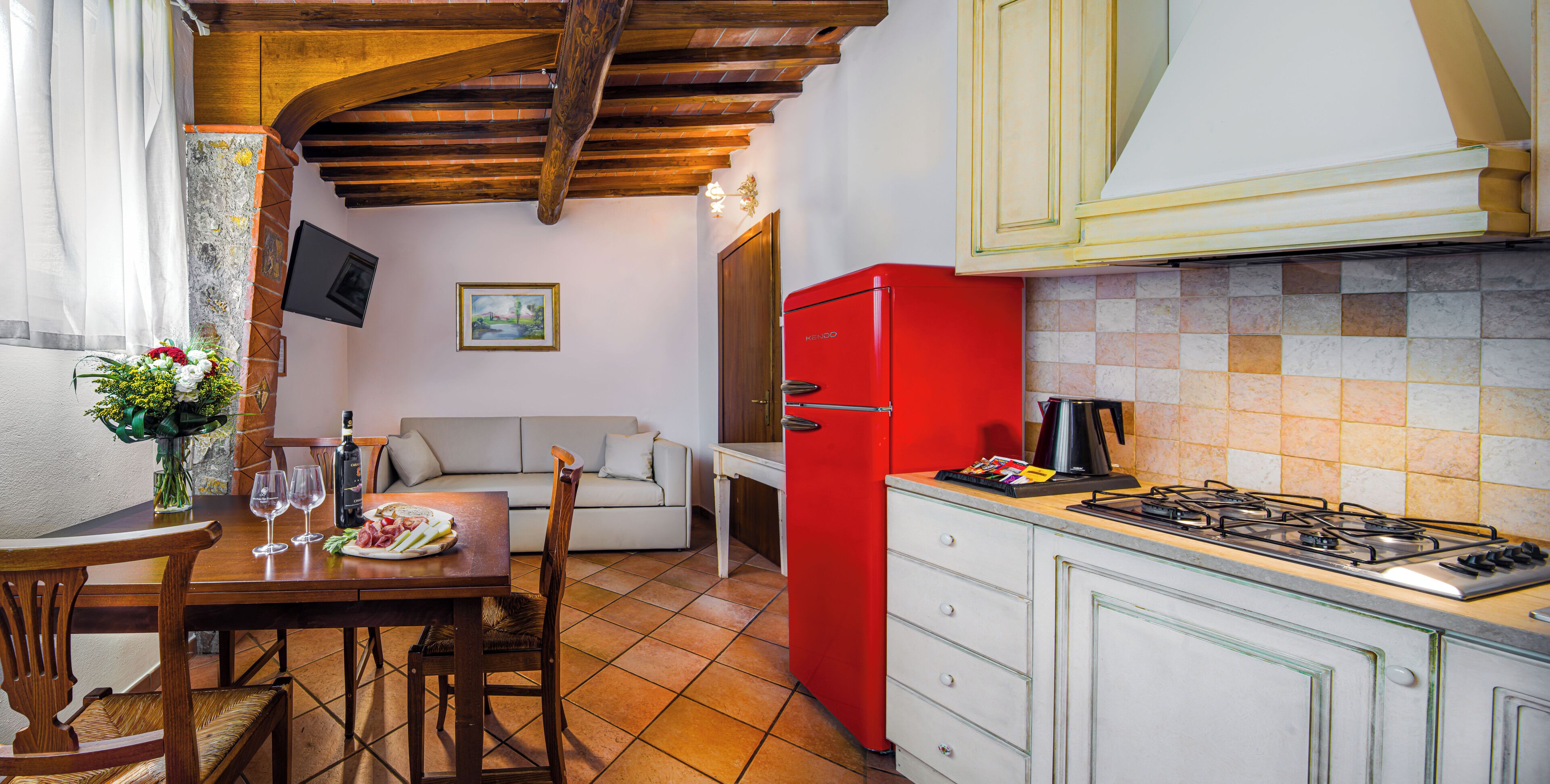 A kitchen with a red refrigerator, a dining table with chairs, and a sofa in the background.