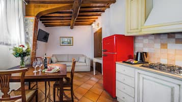 A kitchen with a red refrigerator, a dining table with chairs, and a sofa in the background.
