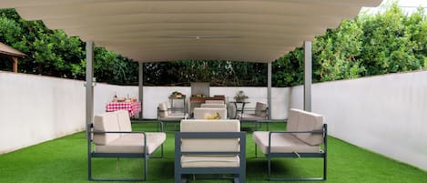 An outdoor patio with a covered seating area, artificial grass, and a table with a red and white checkered tablecloth.