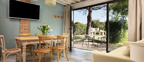 Un comedor con una mesa y sillas, un televisor de pantalla plana montado en la pared y vistas del patio exterior a través de una puerta de cristal.