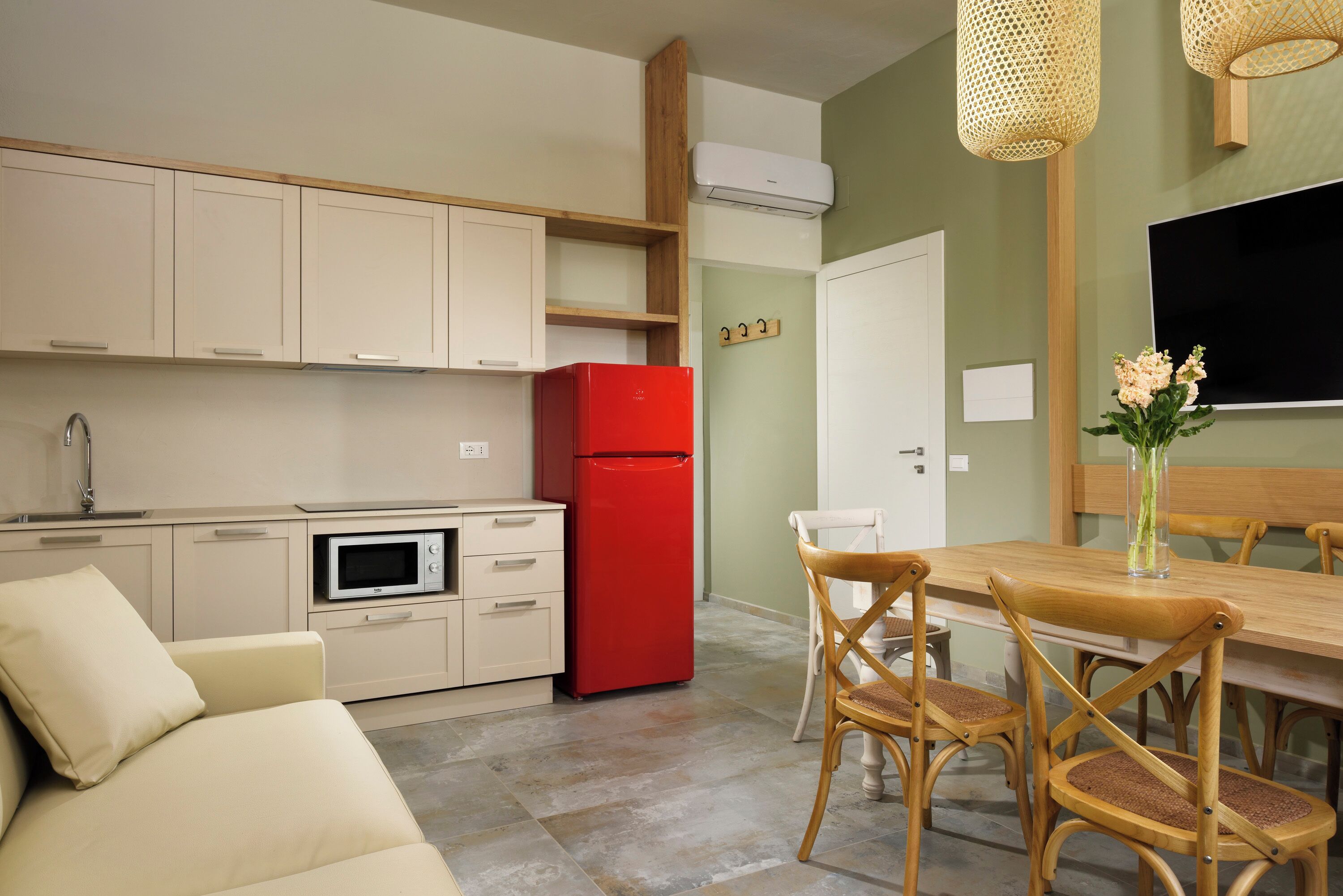 A compact kitchen with a red refrigerator, beige cabinets, and a dining area with wooden chairs and a table.