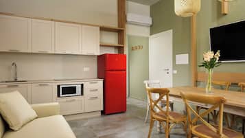 A compact kitchen with a red refrigerator, beige cabinets, and a dining area with wooden chairs and a table.