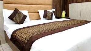 A hotel room with a large bed, a wooden headboard, and a nightstand with a lamp. - Hotel Raghunath (Jammu)