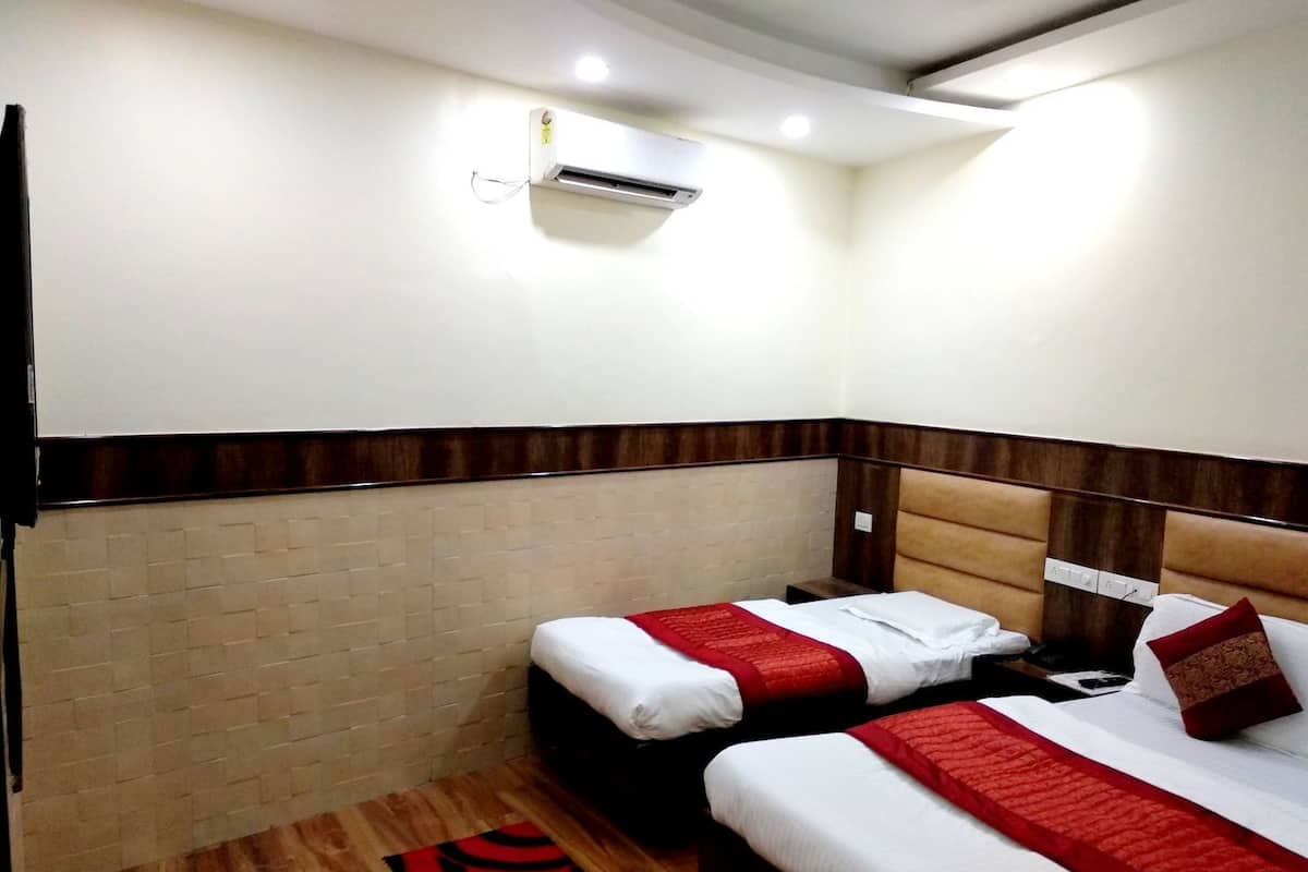 A hotel room with two beds, a red and white bedspread, a wooden floor, a brick wall, and an air conditioning unit.