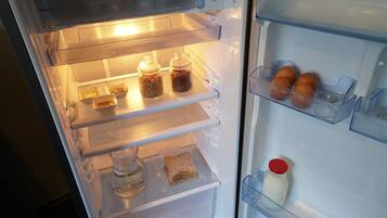 Un refrigerador abierto con repisas que contienen frascos, un cartón de leche y un sándwich.