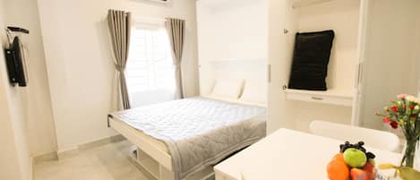 A bedroom with a bed, a bedside table with fruits, a white chair, and a closet with a black towel.