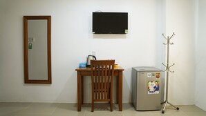A small room with a wooden desk, a chair, a television mounted on the wall, a small refrigerator, and a coat rack. - Happy Homes 95 Le Thi Rieng (Ho Chi Minh City)