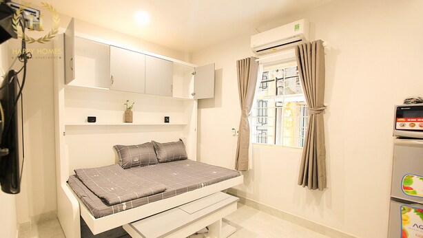 A compact bedroom with a bed, built-in wardrobe, and a window with curtains. - Happy Homes 95 Le Thi Rieng (Ho Chi Minh City)