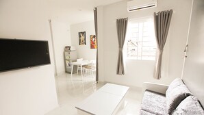 A modern living room with a flat-screen TV, a white sofa, a coffee table, and a dining area with a table and chairs. - Happy Homes 95 Le Thi Rieng (Ho Chi Minh City)