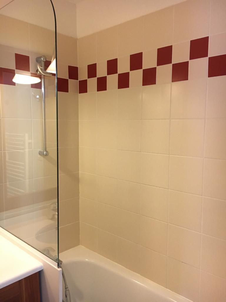 Un bagno con cabina doccia in vetro, una vasca da bagno bianca e una parete rivestita di piastrelle a motivo a scacchi.