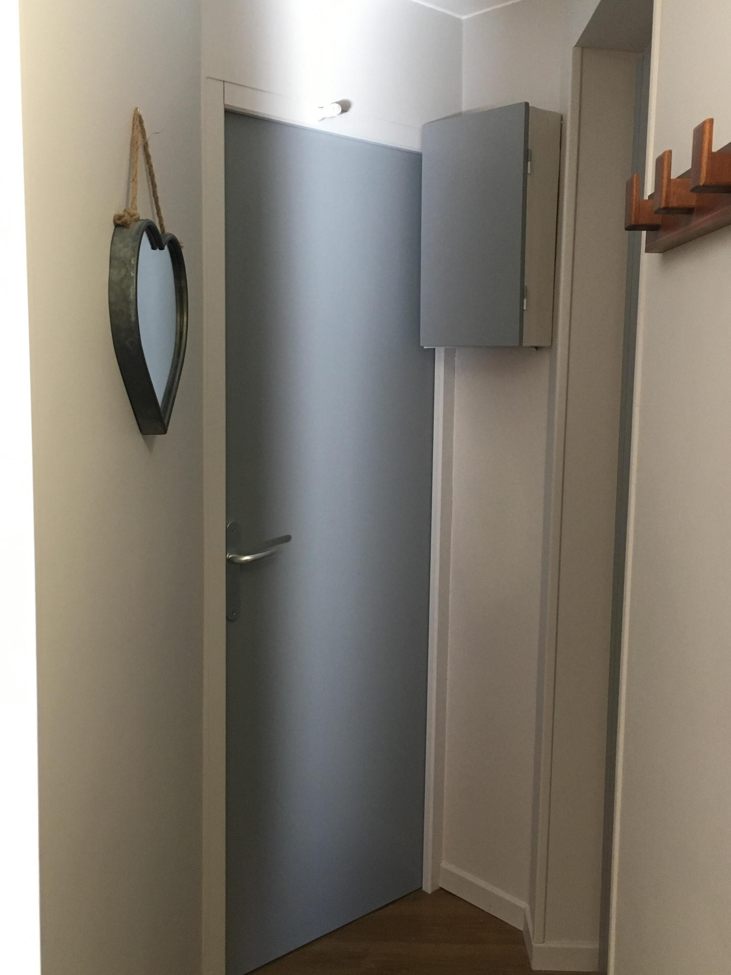 A hallway with a closed door, a small cabinet, and a coat rack.