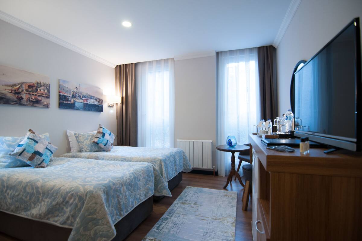 A hotel room with two beds, a television, a small table with a lamp, and artwork on the walls.