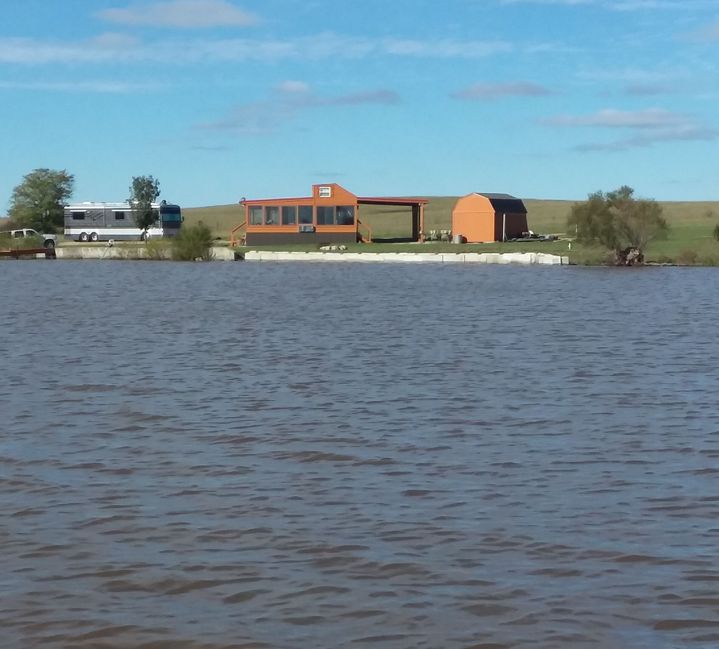 A lakeside property with a large house, a barn, and a trailer.