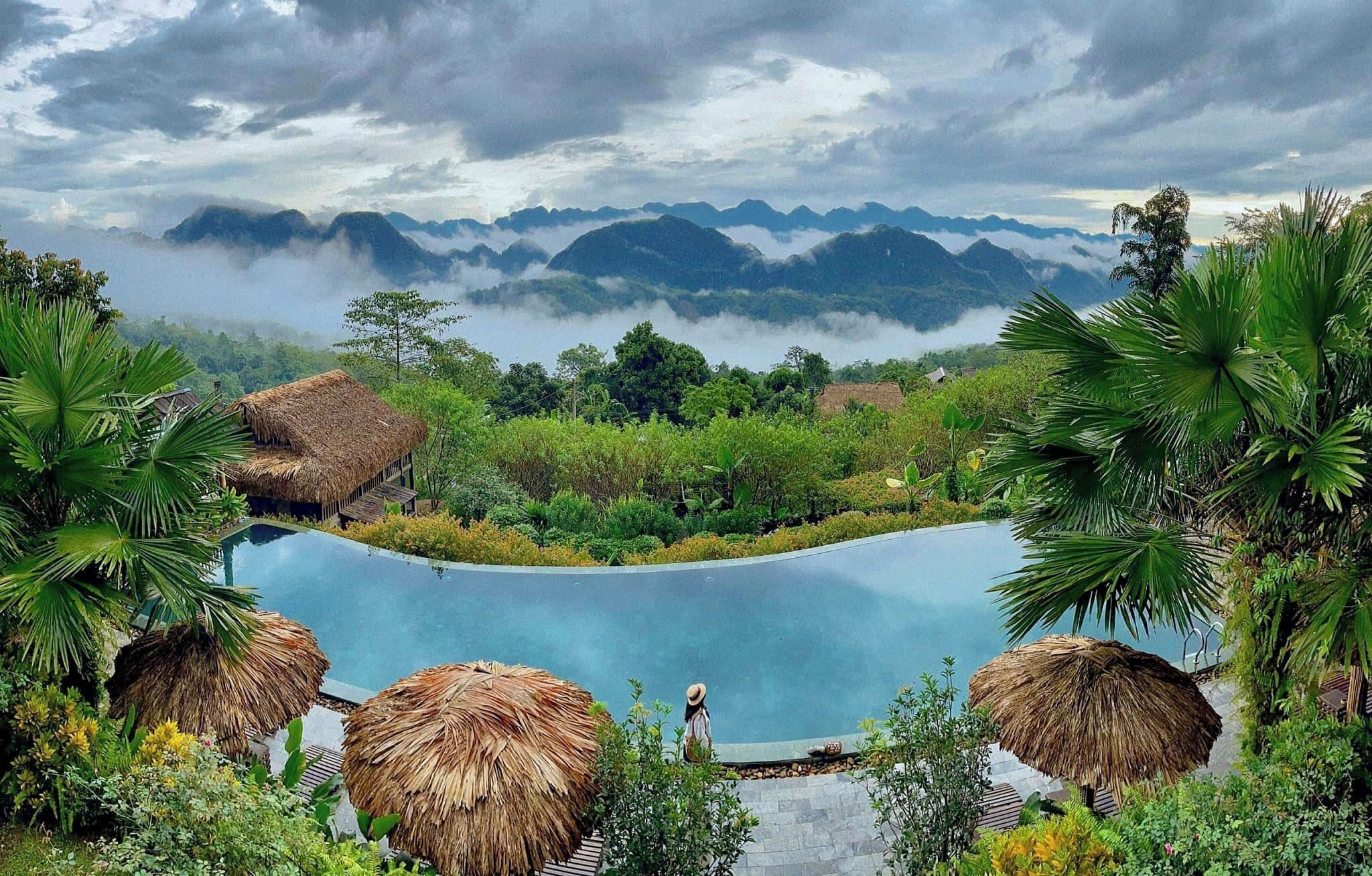 Una piscina rodeada de vegetación tropical y construcciones con techo de paja, con vistas a un paisaje montañoso.