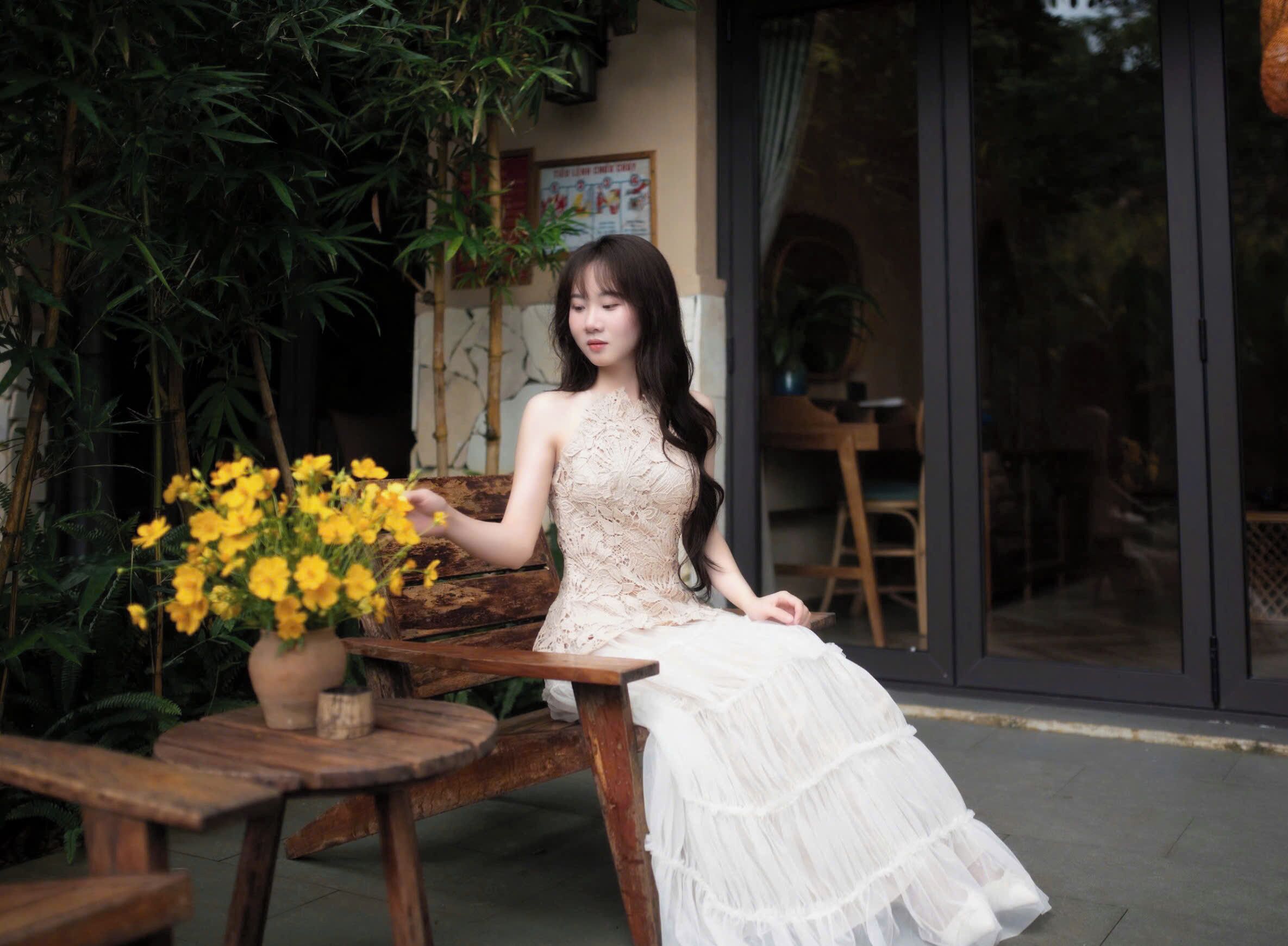 A person seated on a wooden bench outdoors with a potted plant nearby.
