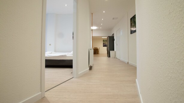 A modern hallway with a wooden floor, a bed in the adjacent room, and a dining area with a table and chairs. - Representative City Villa (Meerbusch)