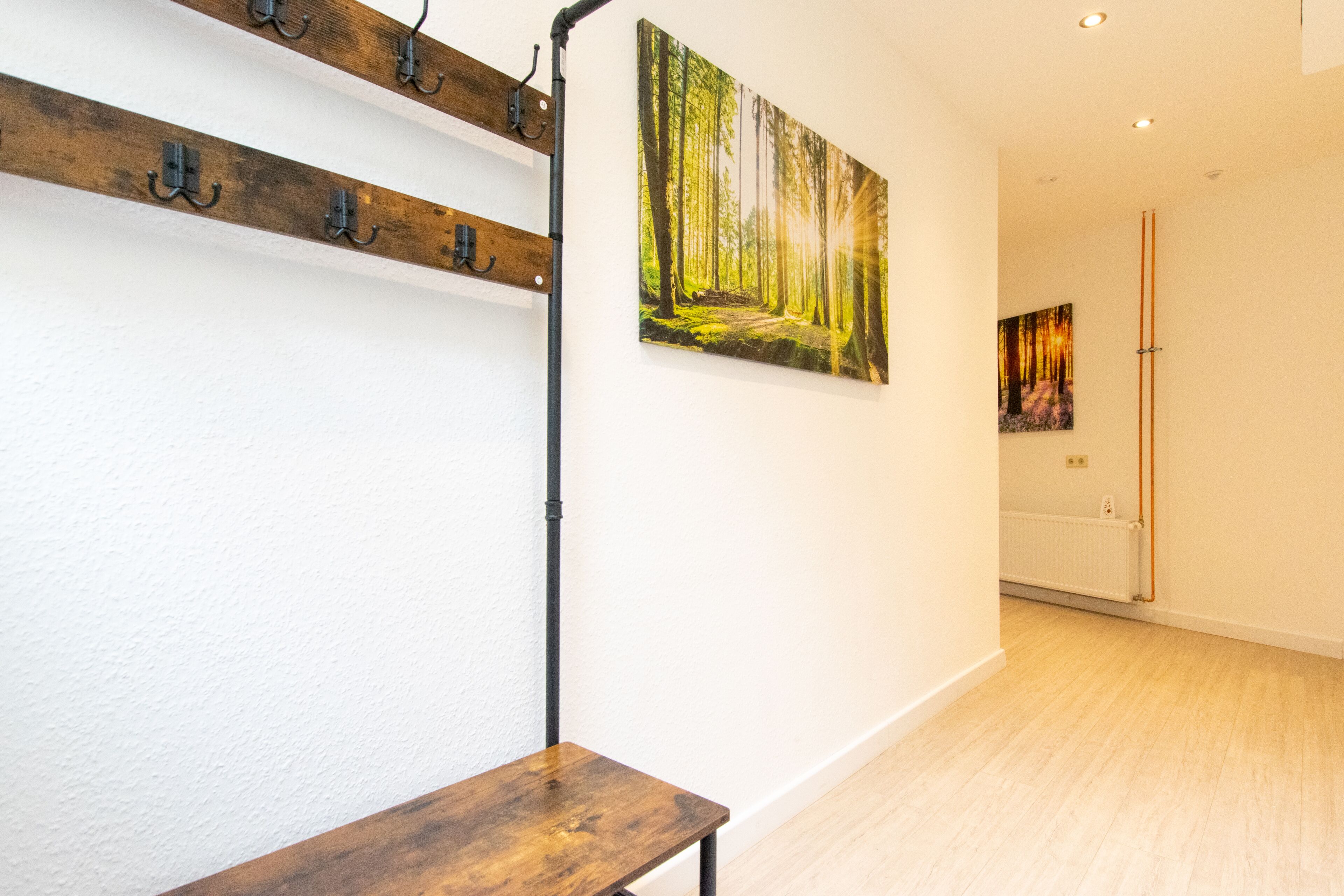 A hallway with a wooden bench, a coat rack, and two paintings on the wall.