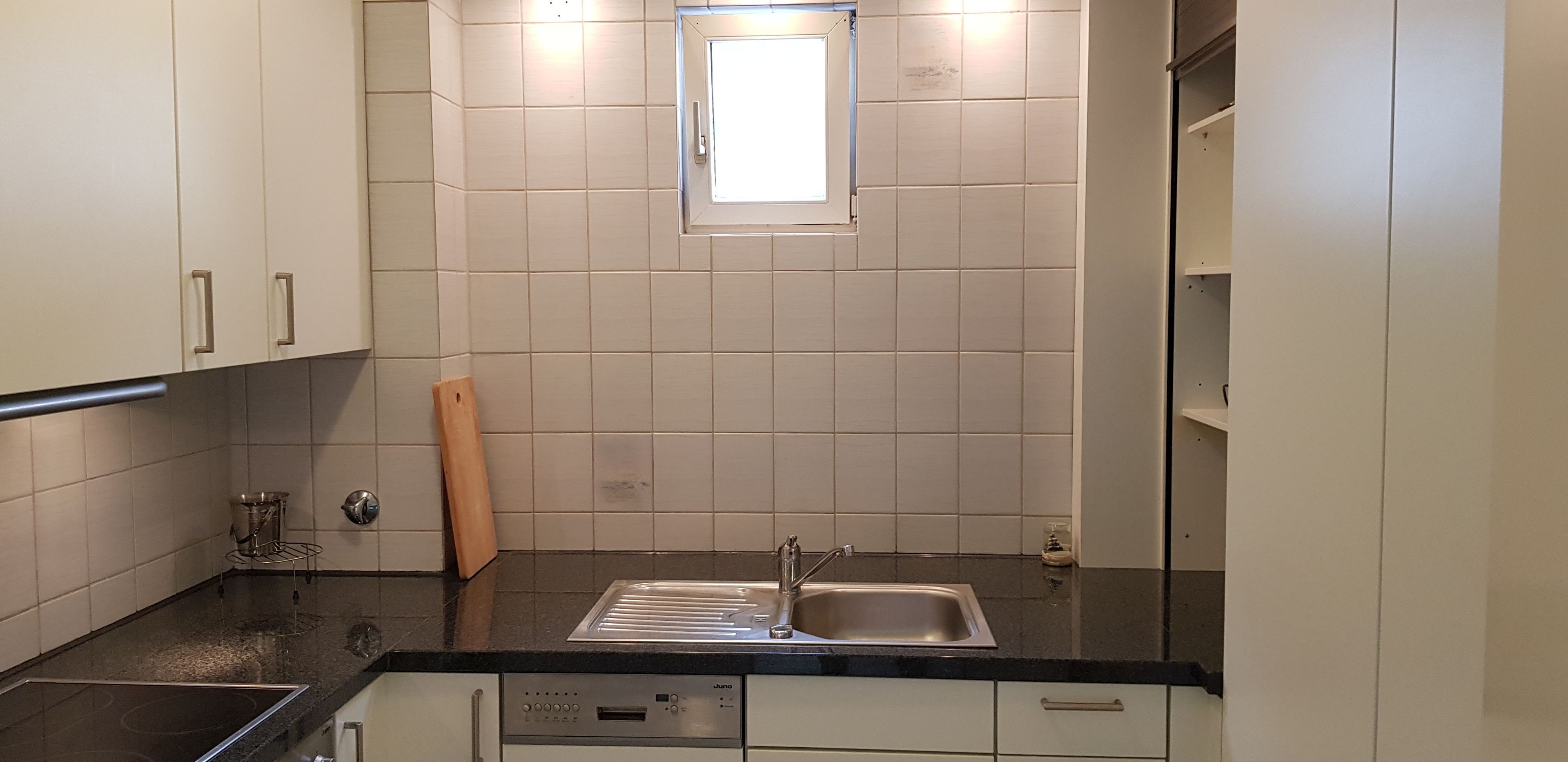 A kitchen with white cabinets, a black countertop, a stainless steel sink, and a window above the sink.
