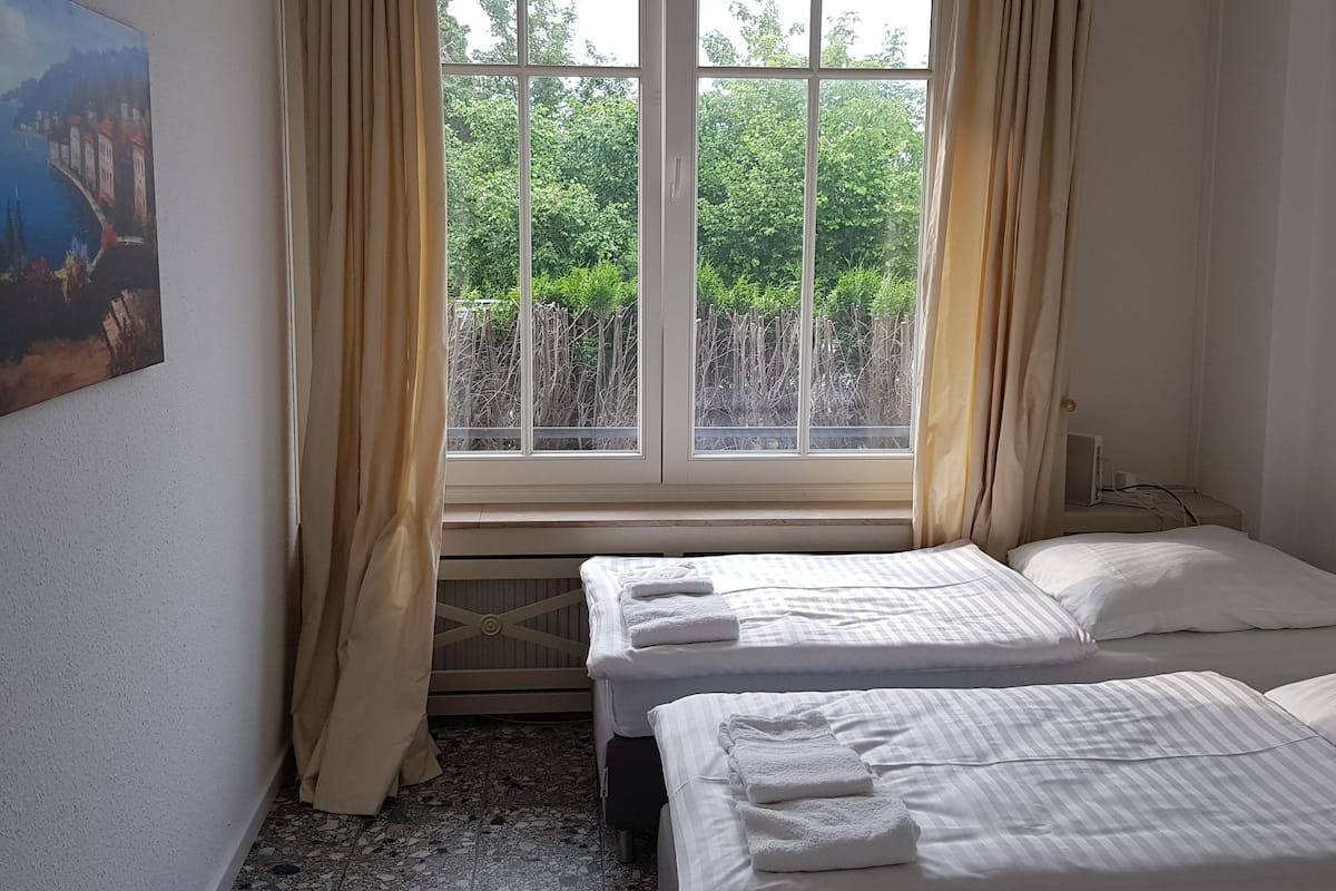 Une chambre avec deux lits, une fenêtre avec des rideaux, un radiateur et un tableau au mur.