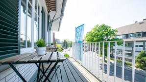 A balcony with a wooden table and chairs, potted plants, and a view of the street and buildings. - Representative City Villa (Meerbusch)