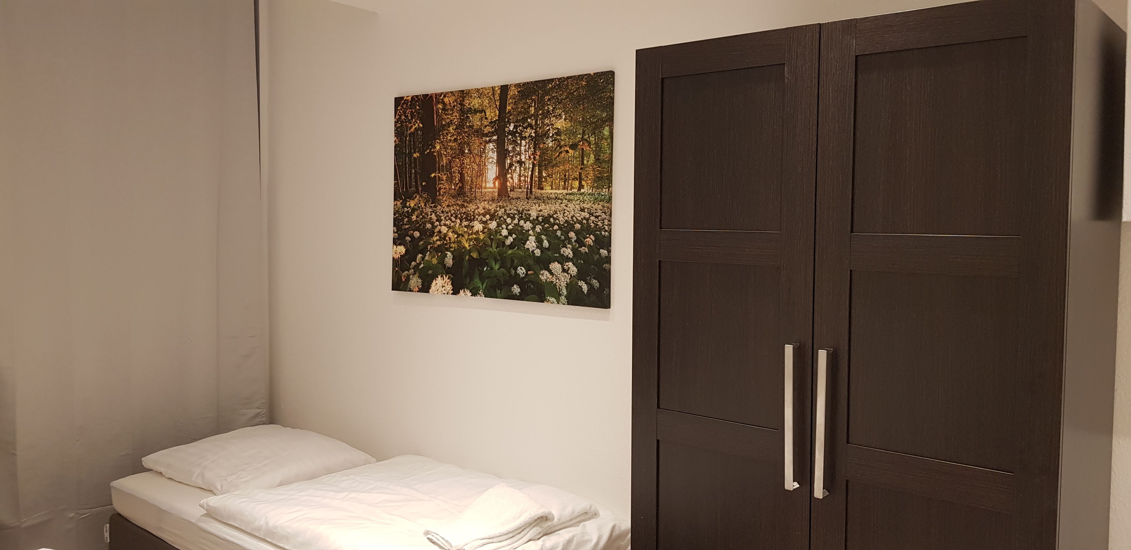 A bedroom with a bed, a wardrobe, and a wall-mounted picture of a forest scene.