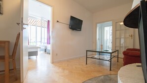 An open-plan living area with a wooden floor, a glass coffee table, a red armchair, and a mounted television. - Representative City Villa (Meerbusch)