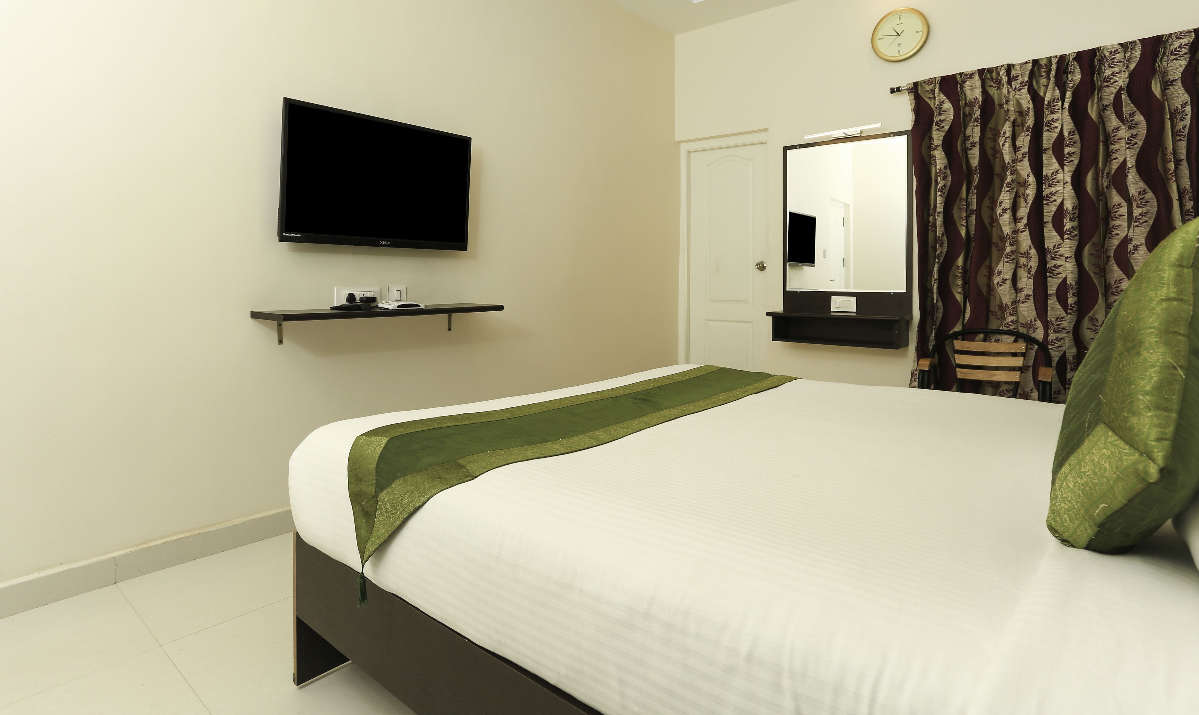 A bedroom with a bed, a television mounted on the wall, a door, and a mirror.