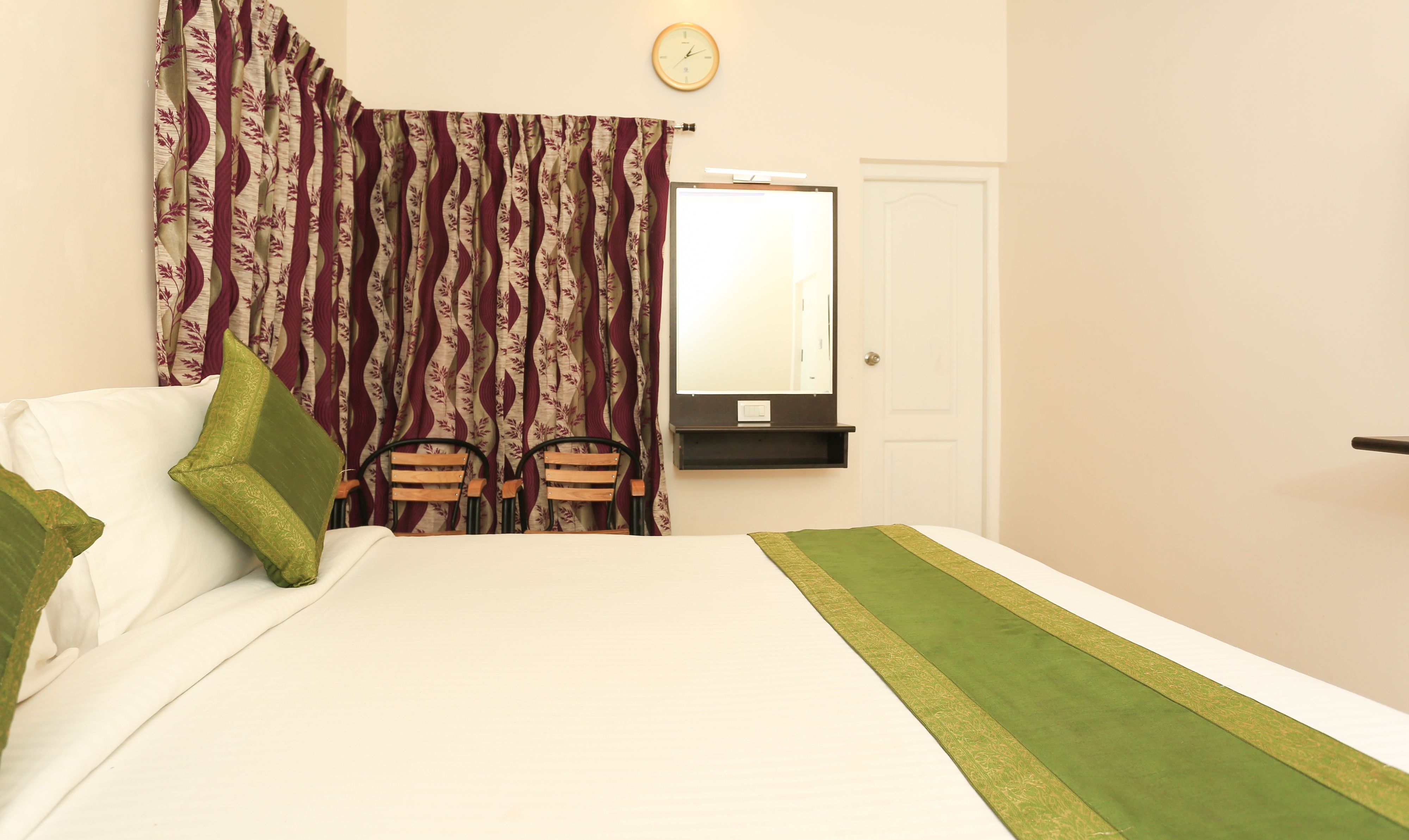 Een keurig opgemaakt slaapkamer met een bed, twee stoelen, een spiegel en een klok aan de muur.