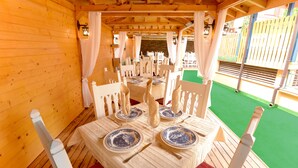 Un coin repas en bois avec des tables dressées pour quatre personnes, des chaises blanches et des assiettes bleues et blanches.