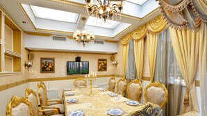 Une salle à manger élégante, avec une longue table, des chaises richement décorées et un lustre.