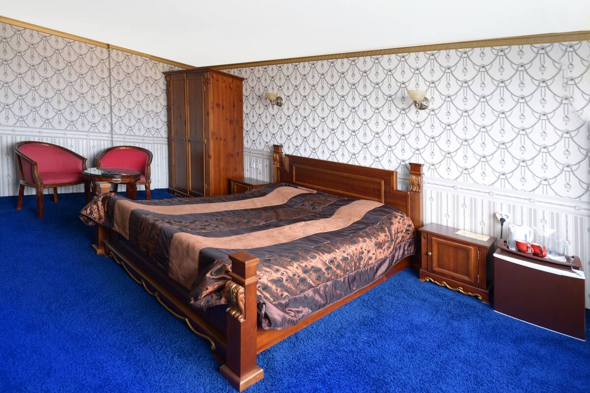 Ein Schlafzimmer mit einem hölzernen Bett, zwei roten Stühlen, einem Nachttisch und einer Wand mit Muster.