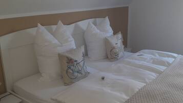 A neatly made bed with white bedding and several pillows, including one with a bicycle design.