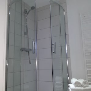 Une douche fermée par des parois en verre, dotée d’un pommeau de douche à main et d’un panneau de commande fixé au mur.
