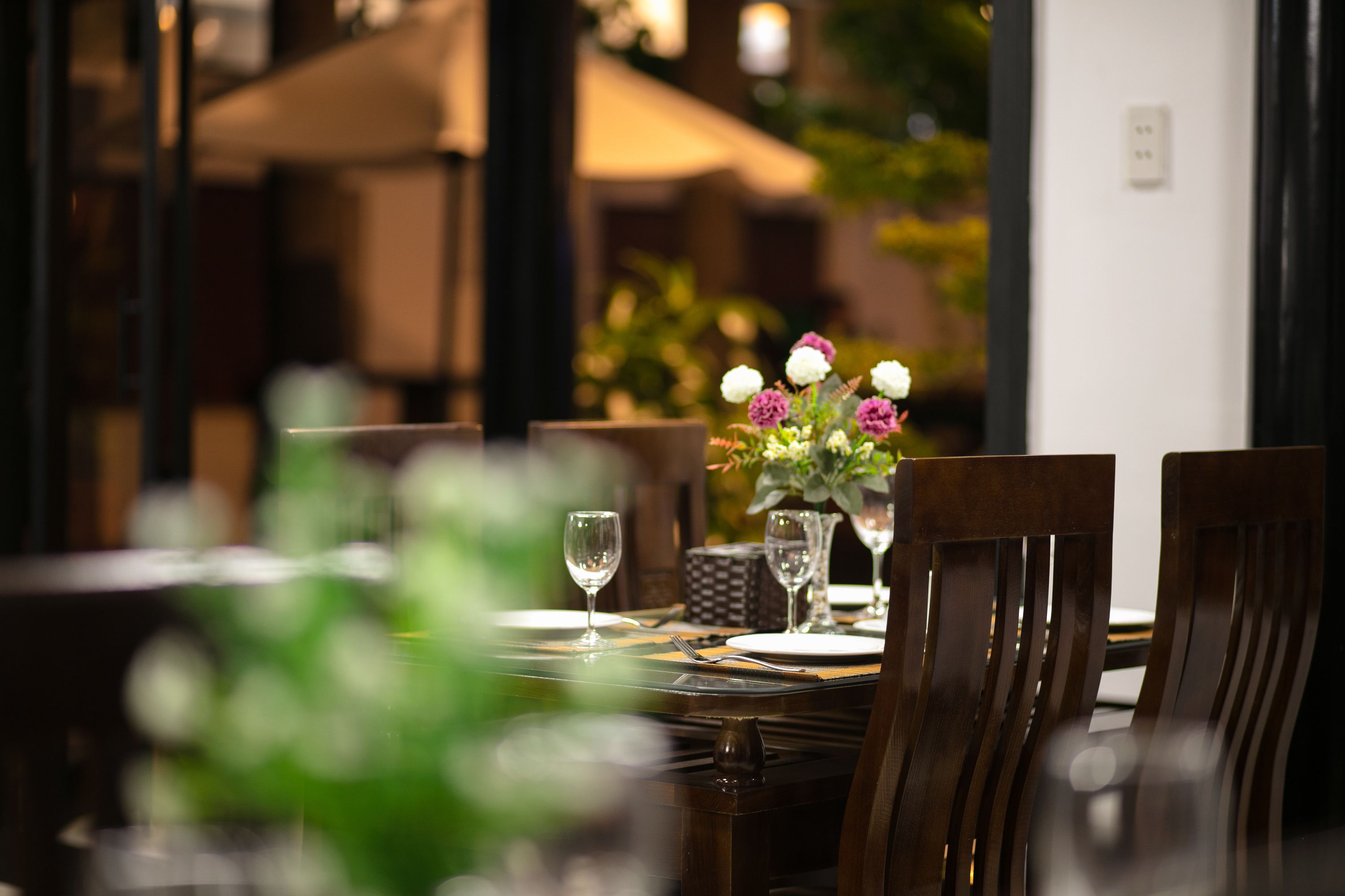 A dining table set with chairs, a vase with flowers, and wine glasses.