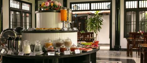 Montaje de bufé con diferentes alimentos y bebidas, como frutas, pastelería y una estación de café.
