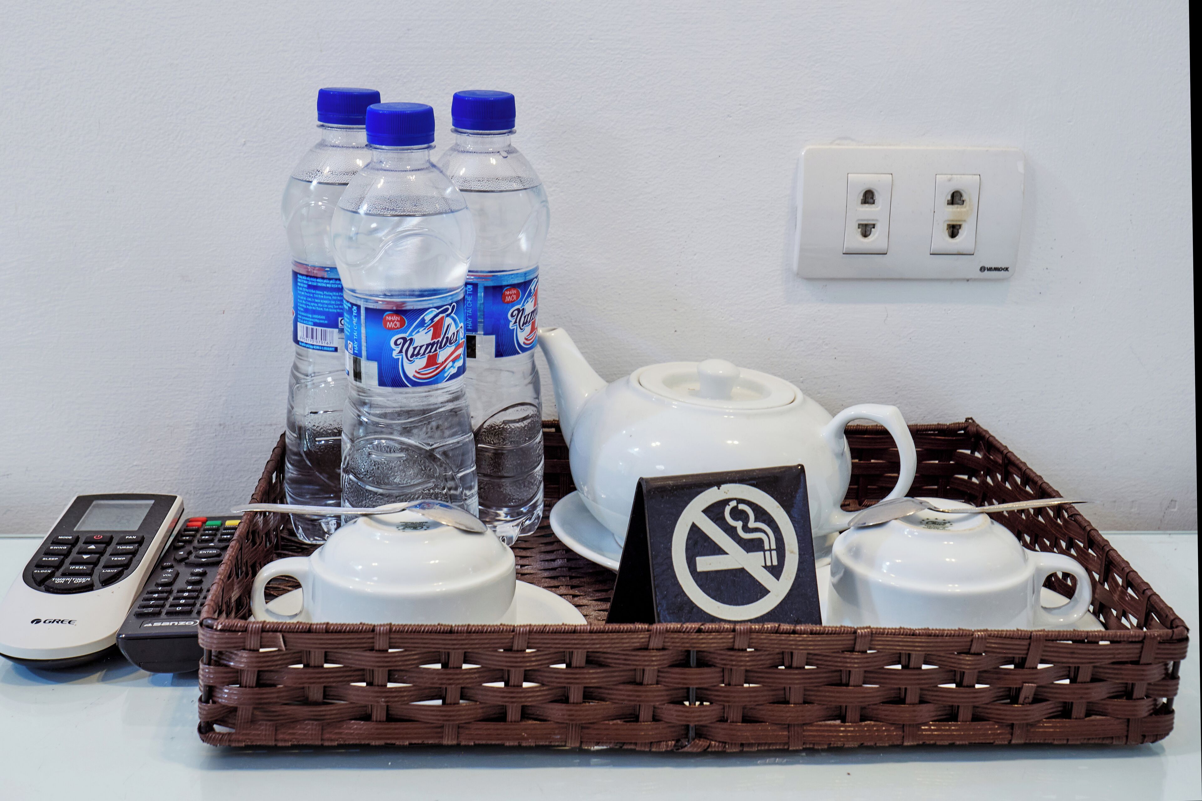 A wicker tray with a teapot, cups, a no-smoking sign, a calculator, and bottled water.