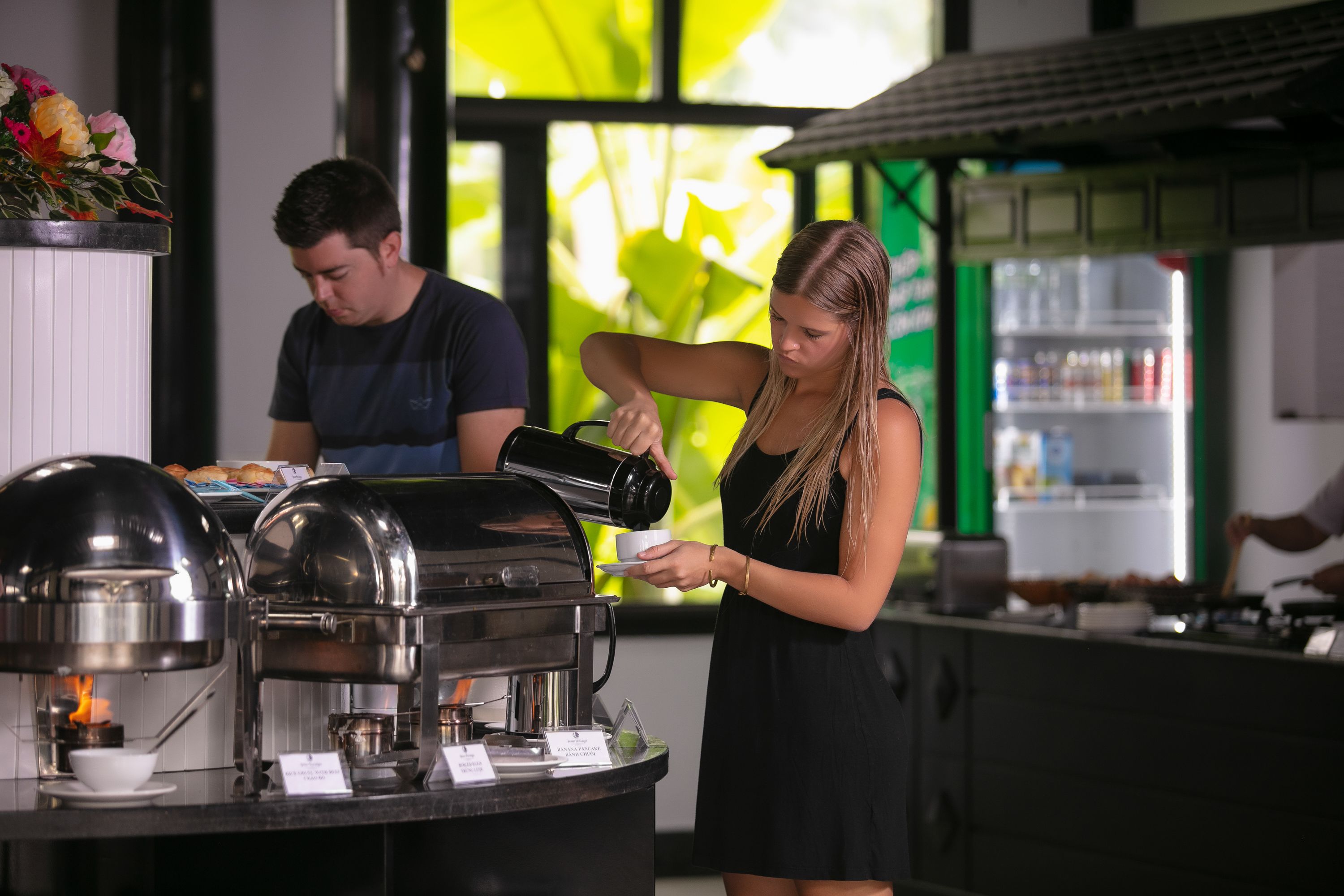 A buffet setup with a coffee station, a counter with food items, and a person serving coffee.