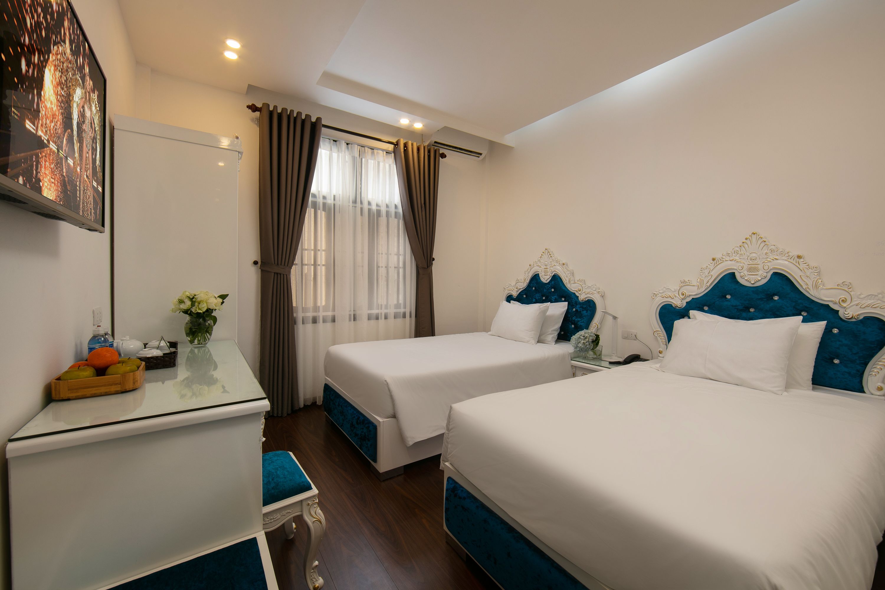 A hotel room with two beds, a desk, a TV, and a window with curtains.