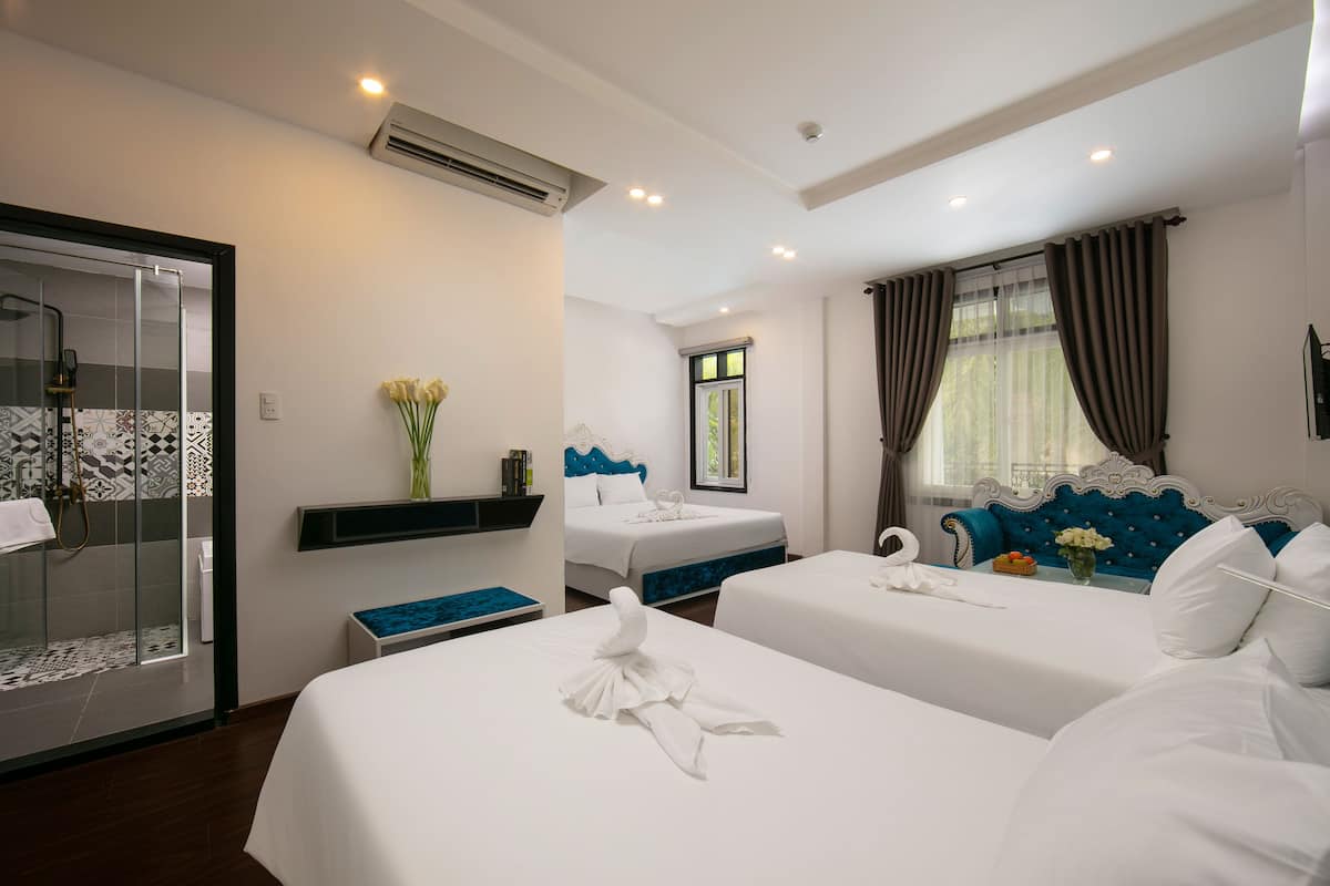 A hotel room with a shower, two beds, a blue headboard, and a window with curtains.