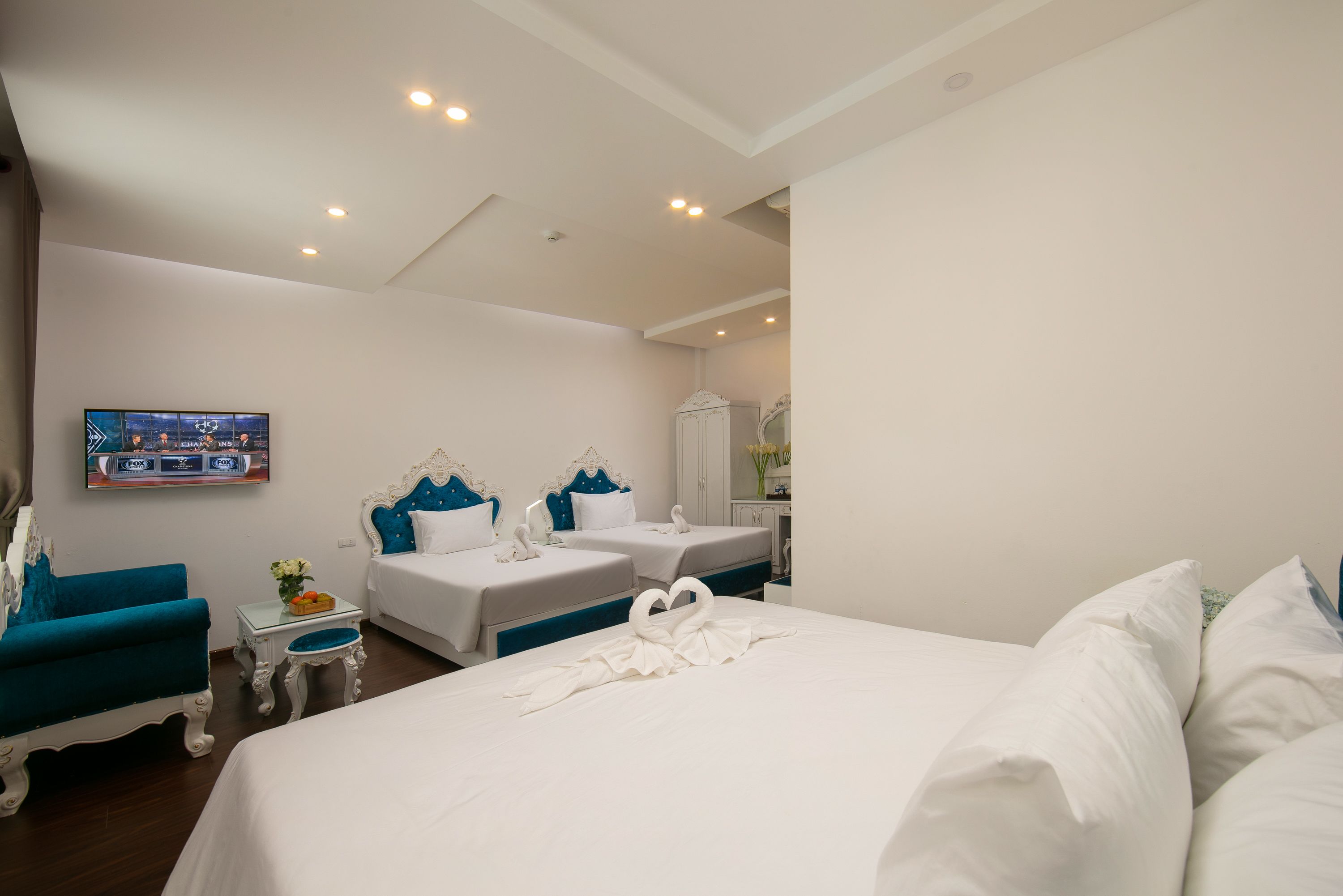 Habitación de hotel con dos camas, televisión, una mesita con flores y un espejo.
