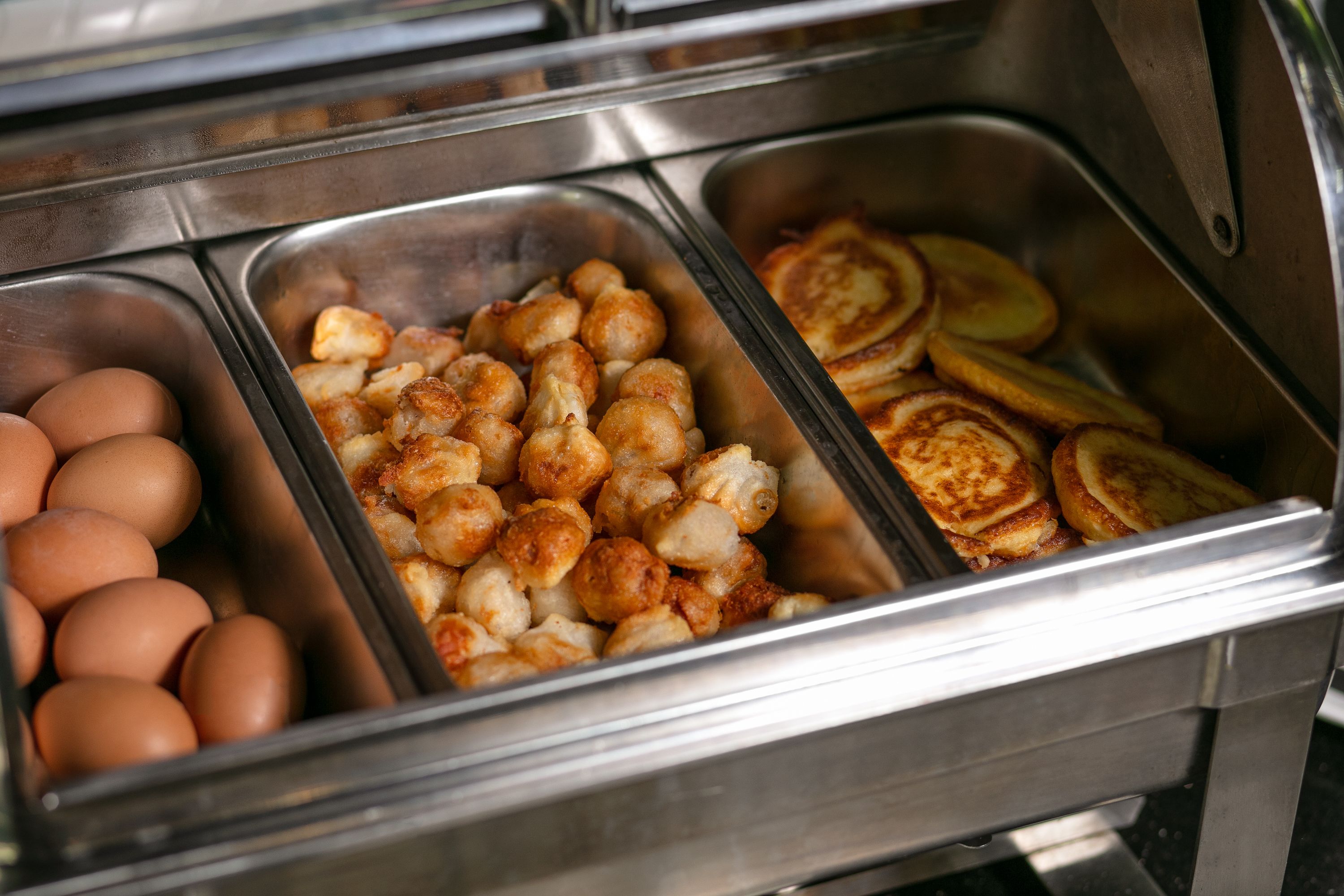 Un bufé con bandejas de huevos, nuggets de pollo y panqueques.