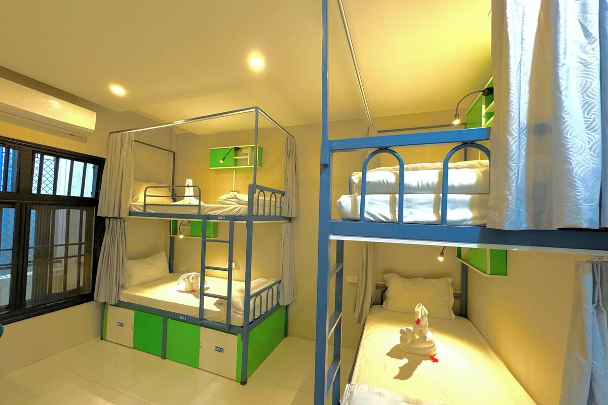 A room with bunk beds, a green cabinet, a window with curtains, and a bedside table with a lamp.